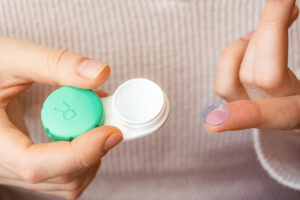 the girl is holding a container for soft contact lenses and a lens on her finger